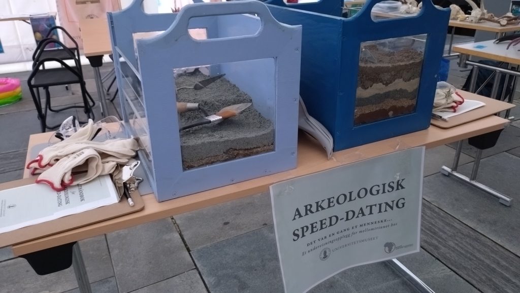 Gravebokser for aspirernde arekeologer; to bokser på et bord med plexiglass på disene sp en kan se ulike sedimentlag nedover. Oppi boksen er grus en kan grave i for å finne artefakter