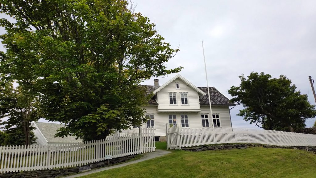 Villa Vibrandsøy, en hvit trevilla med hvitt stakittgjernde og store trær i hagen
